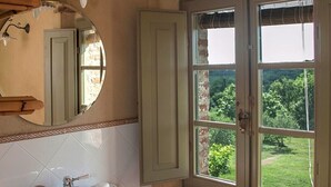 A bathroom with a white sink, a mirror, and a window with a view of greenery.