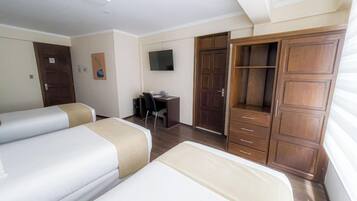 Ein Hotelzimmer mit zwei Betten, einem Schreibtisch, einem Fernseher und einem Kleiderschrank.