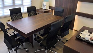 A conference room with a long table, six chairs, a water dispenser, and a coffee service tray.