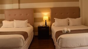 Habitación de hotel con dos camas, una mesita de noche con lámpara y paredes a rayas.