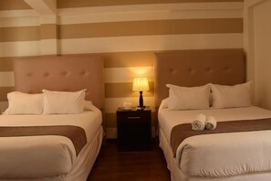 A hotel room with two beds, a nightstand with a lamp, and striped walls.