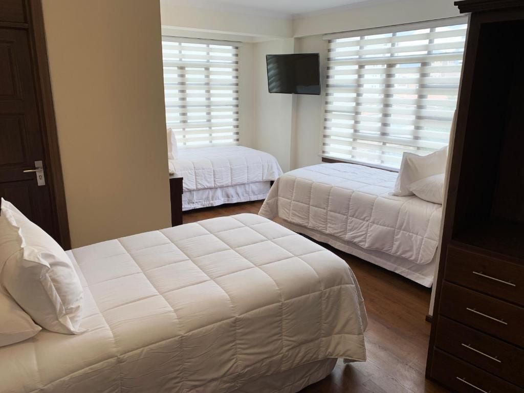 A hotel room with two beds, a TV mounted on the wall, and a wooden wardrobe.
