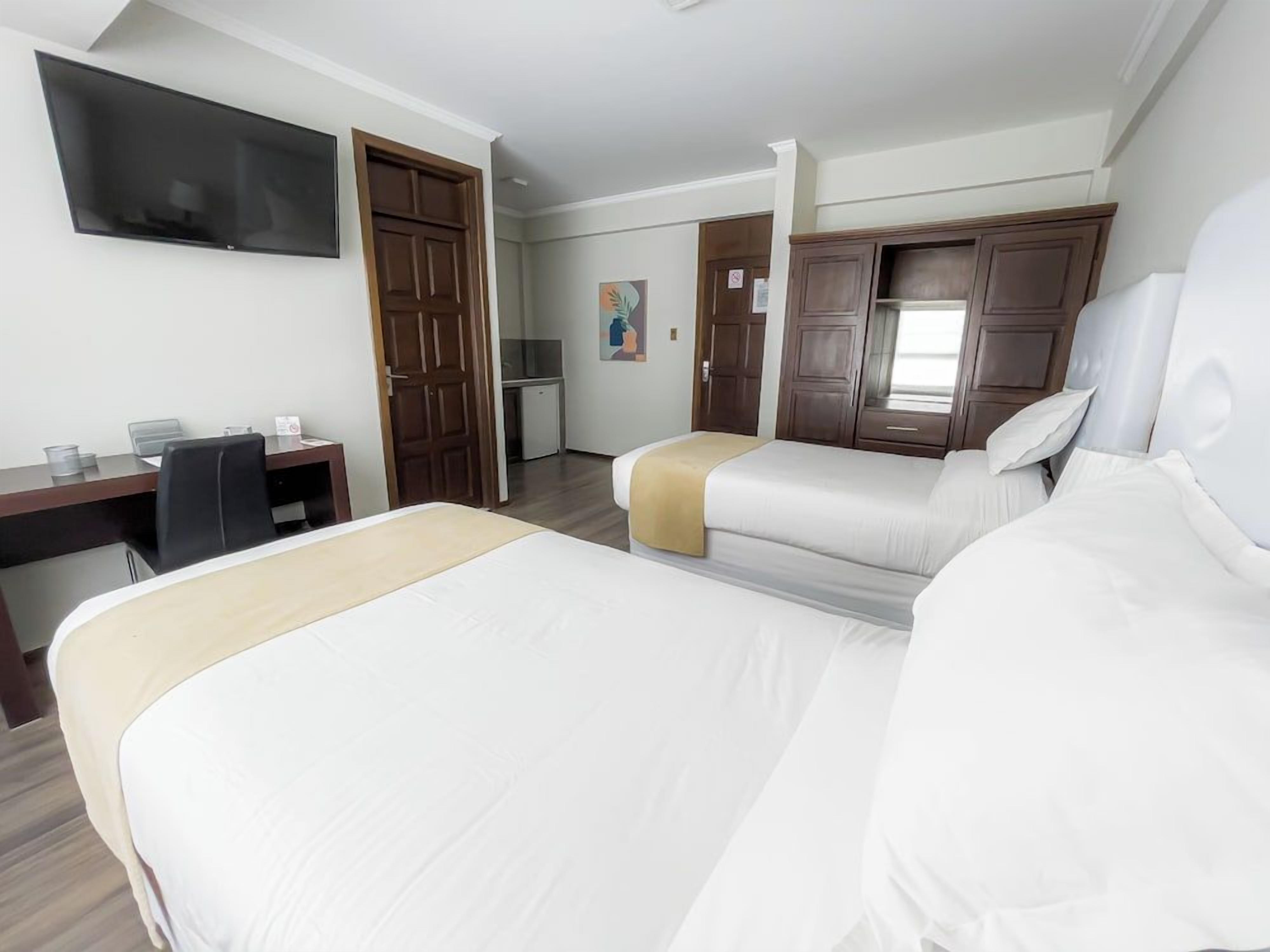 Habitación de hotel con dos camas, un escritorio, un televisor y un armario.