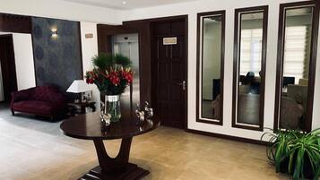 A lobby with a round table, a sofa, a vase with flowers, and a door with a sign.
