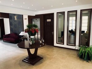 Un hall con una mesa redonda, un sofá, un jarrón con flores y una puerta con un letrero.