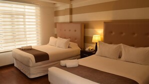 A hotel room with two beds, a nightstand with a lamp, and a window with blinds. - Hotel Boutique Domani (Cochabamba)