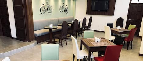 A restaurant with a seating area, tables, chairs, a television, and a wall-mounted bicycle.