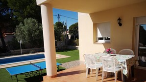 Un patio con mesa y sillas, piscina y césped.