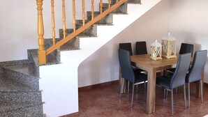 Una escalera con barandillas de madera que conduce a un área de comedor con una mesa y sillas de madera, y dos faroles sobre la mesa.