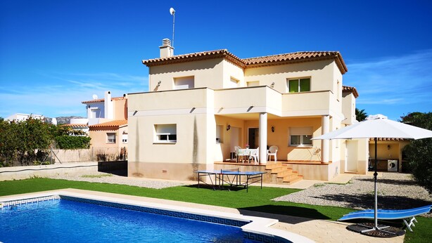Una casa de dos pisos con piscina, mobiliario exterior y un patio cubierto.