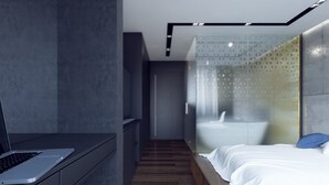 Un dormitorio moderno con suelo de madera, una cama con ropa blanca, un ordenador portátil sobre un escritorio y un separador de vidrio con un diseño geométrico.