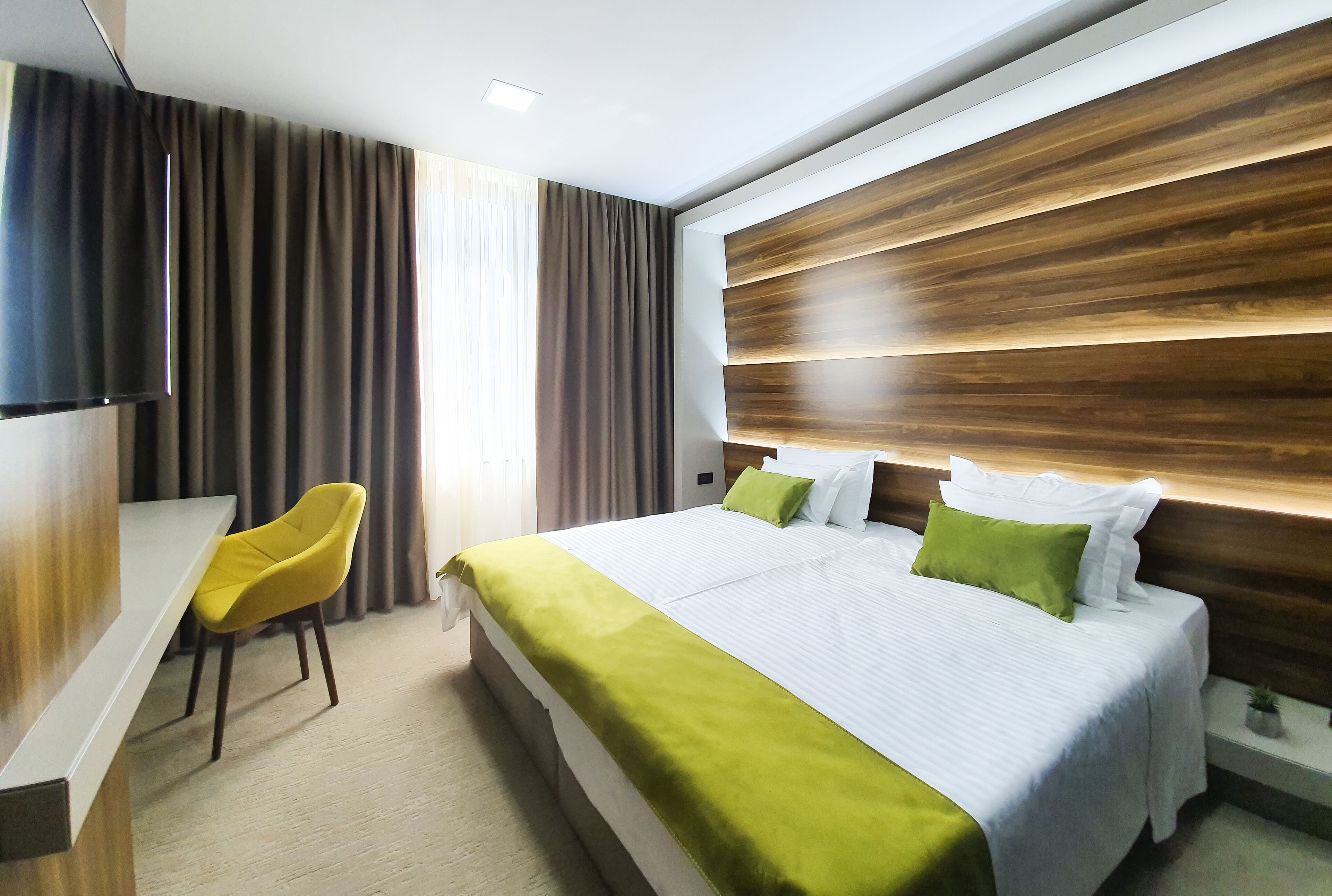 A modern hotel room with a large bed, a desk, and a television.