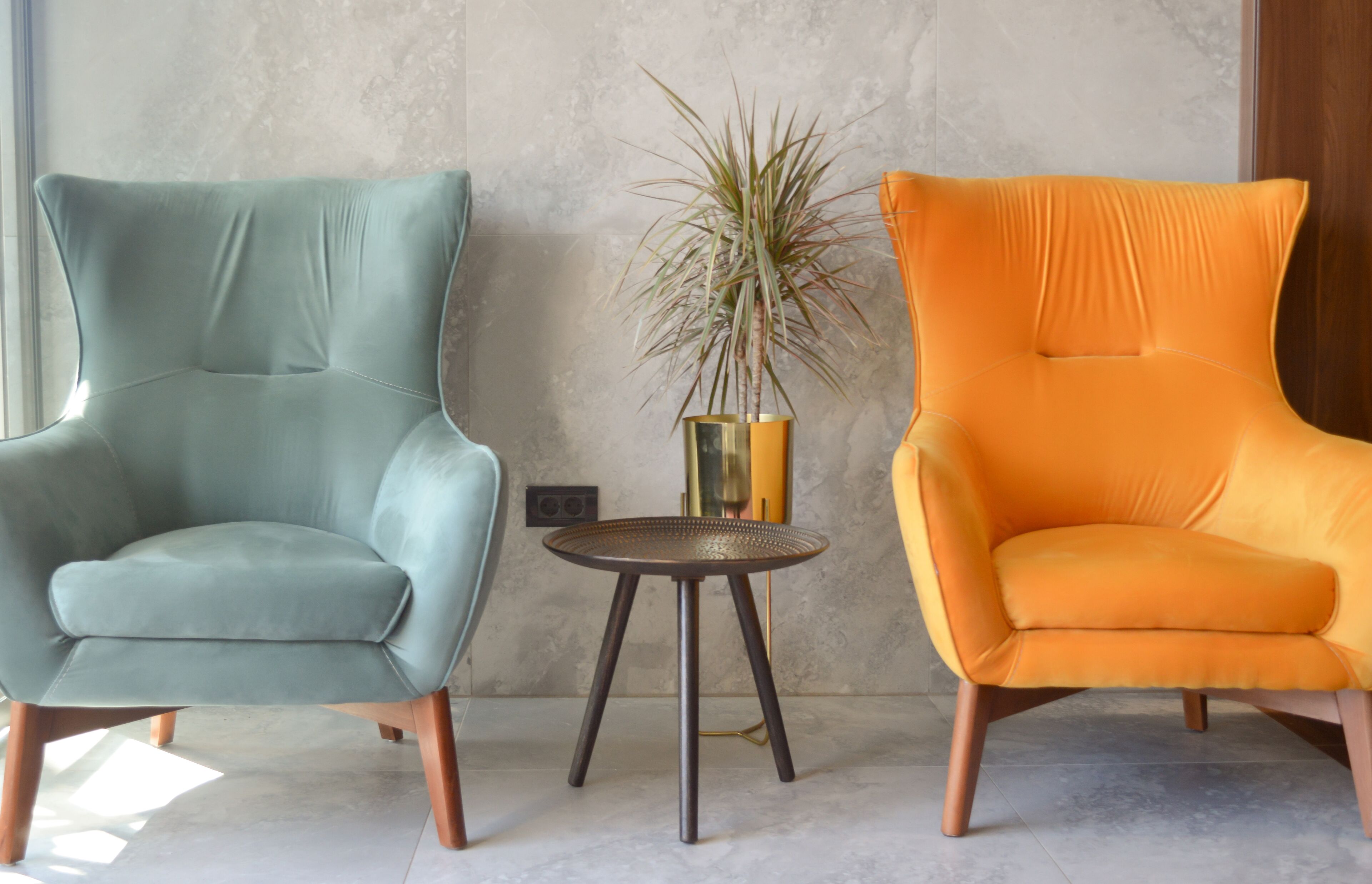 Two armchairs in teal and orange, a small round table with a plant, and a textured wall.