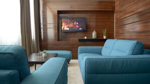 Una sala de estar moderna con un televisor montado en una pared de madera, un sofá azul, un reposapiés a juego y una mesita con objetos decorativos.