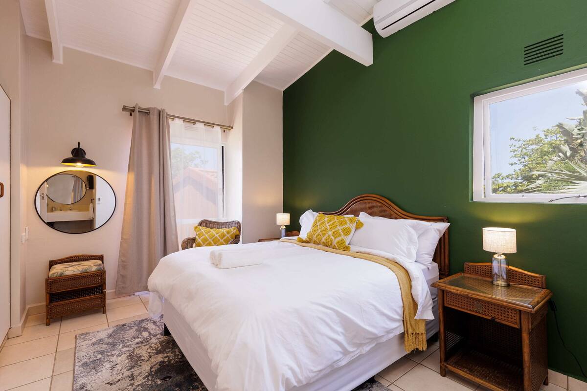 Une chambre bien rangée, avec un grand lit, des lampes de chevet, une petite table, un miroir et une vue sur l’extérieur.