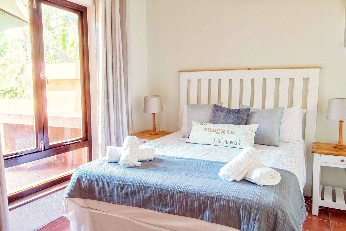 Une chambre à coucher avec un lit, des oreillers, une table de chevet et une fenêtre.