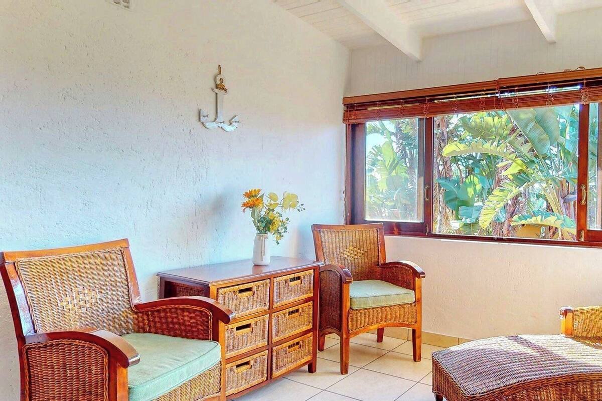 Une pièce meublée de mobilier en osier, une fenêtre donnant sur un paysage verdoyant et un luminaire fixé au mur.