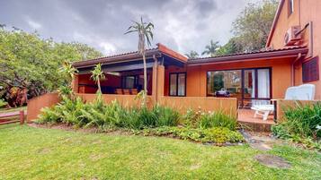 A modern house with a covered patio, a barbecue area, and a lush garden.