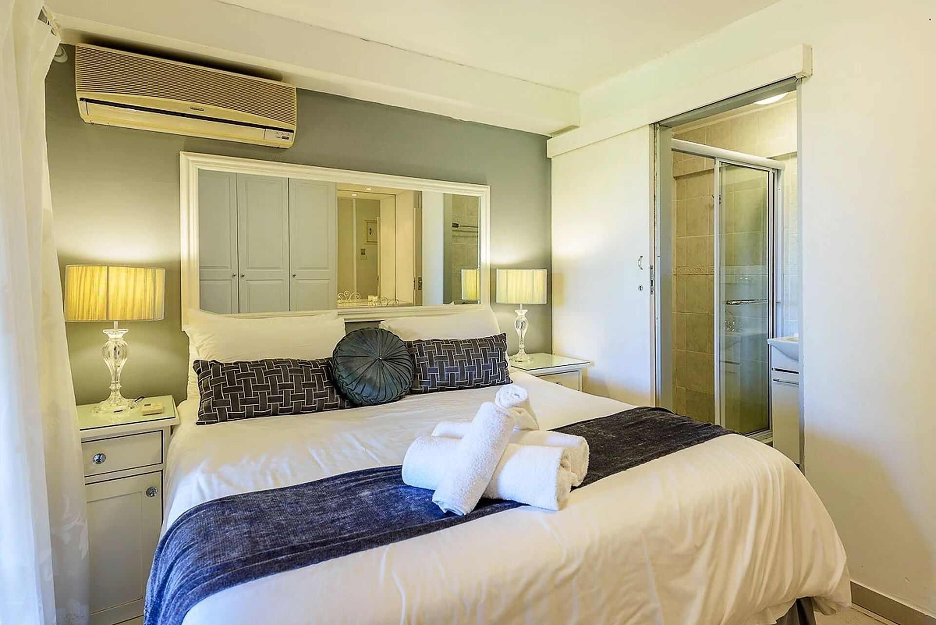 Een hotelkamer met een bed, nachtkastje, lamp, spiegel en douche.