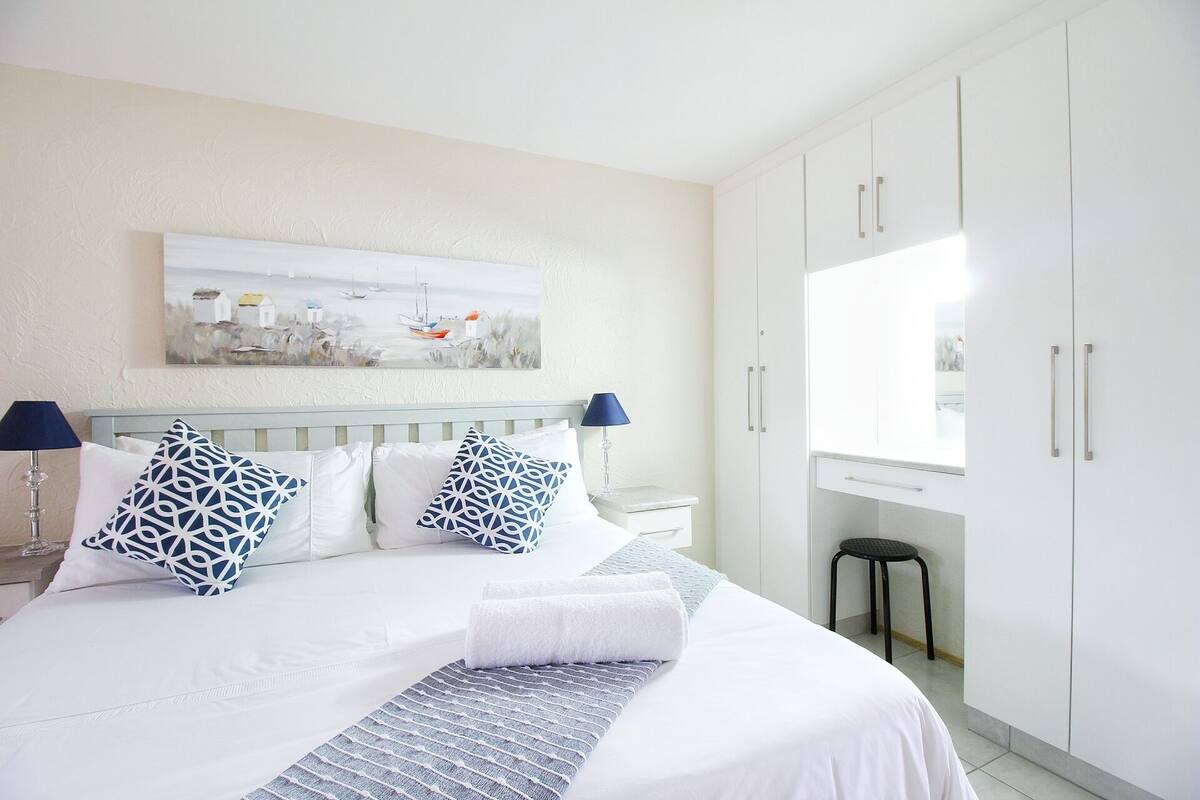 Une chambre bien rangée, avec un grand lit, une table de chevet, une chaise et une armoire.