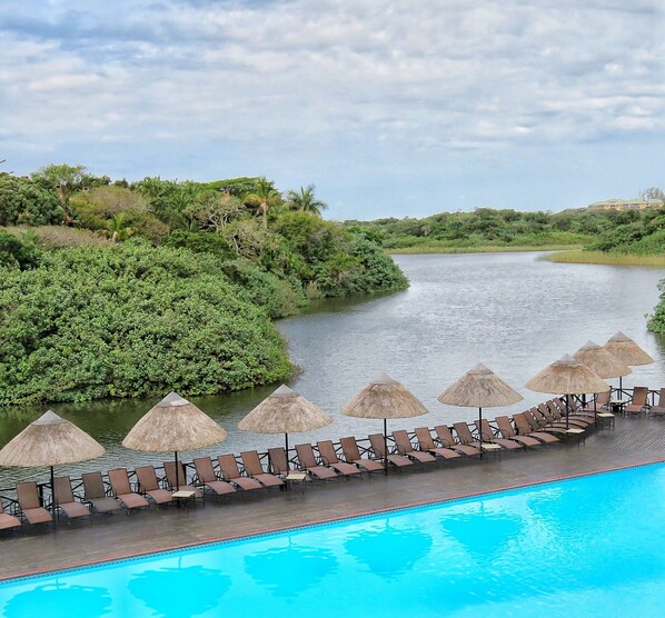 Relax by the serene pool overlooking the river, surrounded by lush greenery and comfortable lounge chairs.