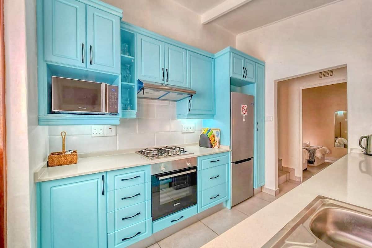 Une cuisine avec des meubles de rangement bleus, un four à micro-ondes, une cuisinière et un réfrigérateur.