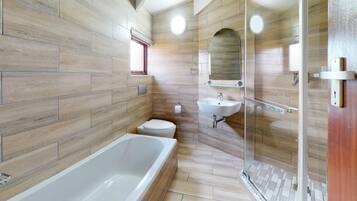 Een moderne badkamer met een bad, toilet en een douchecabine met glazen wanden.