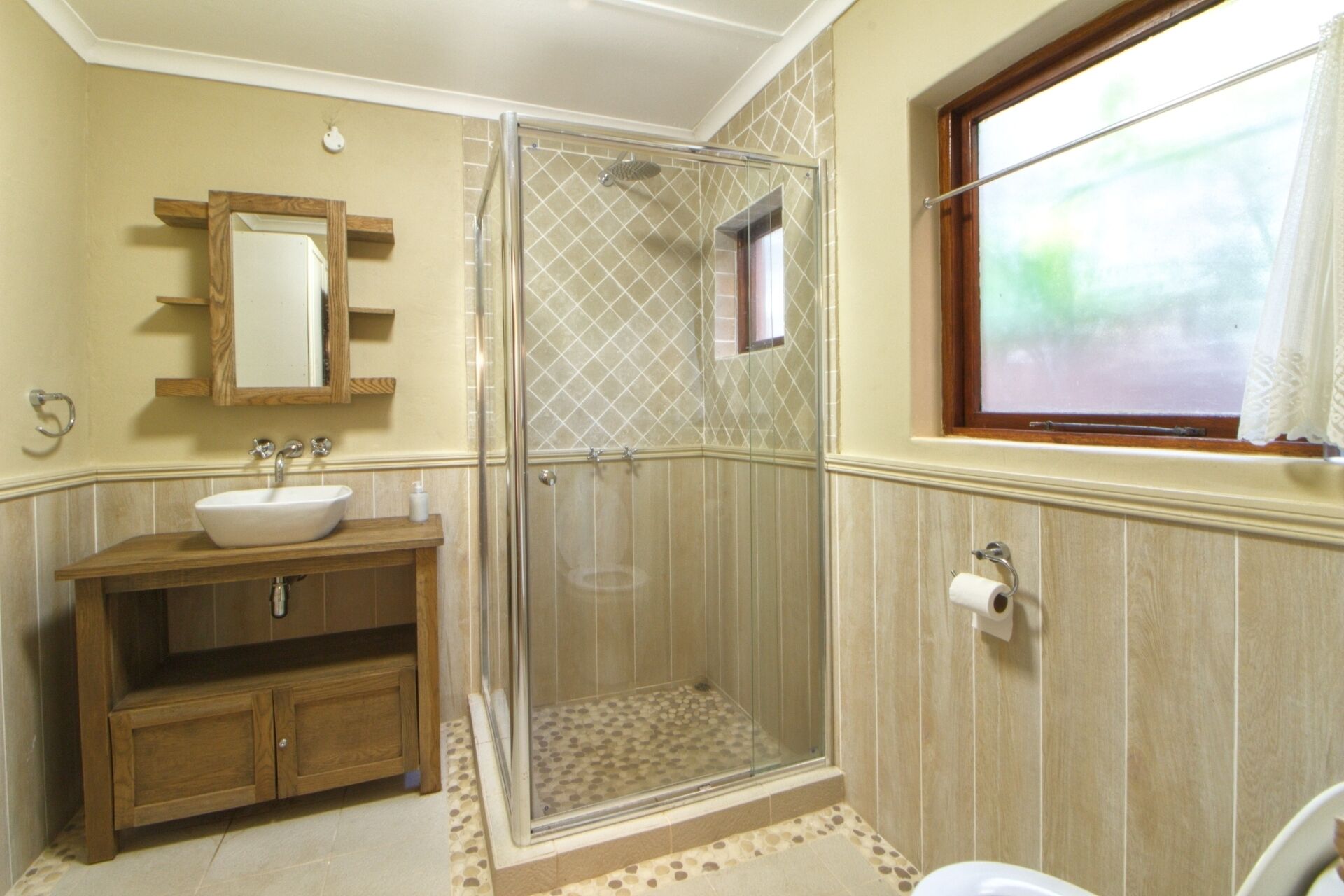 Une salle de bain avec une douche à parois de verre, un meuble-lavabo en bois, un miroir et une fenêtre.