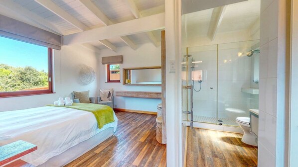 A modern bedroom with a large bed, a view of the outdoors, a glass shower, and a small seating area. - San Lameer by Top Destinations (Southbroom)