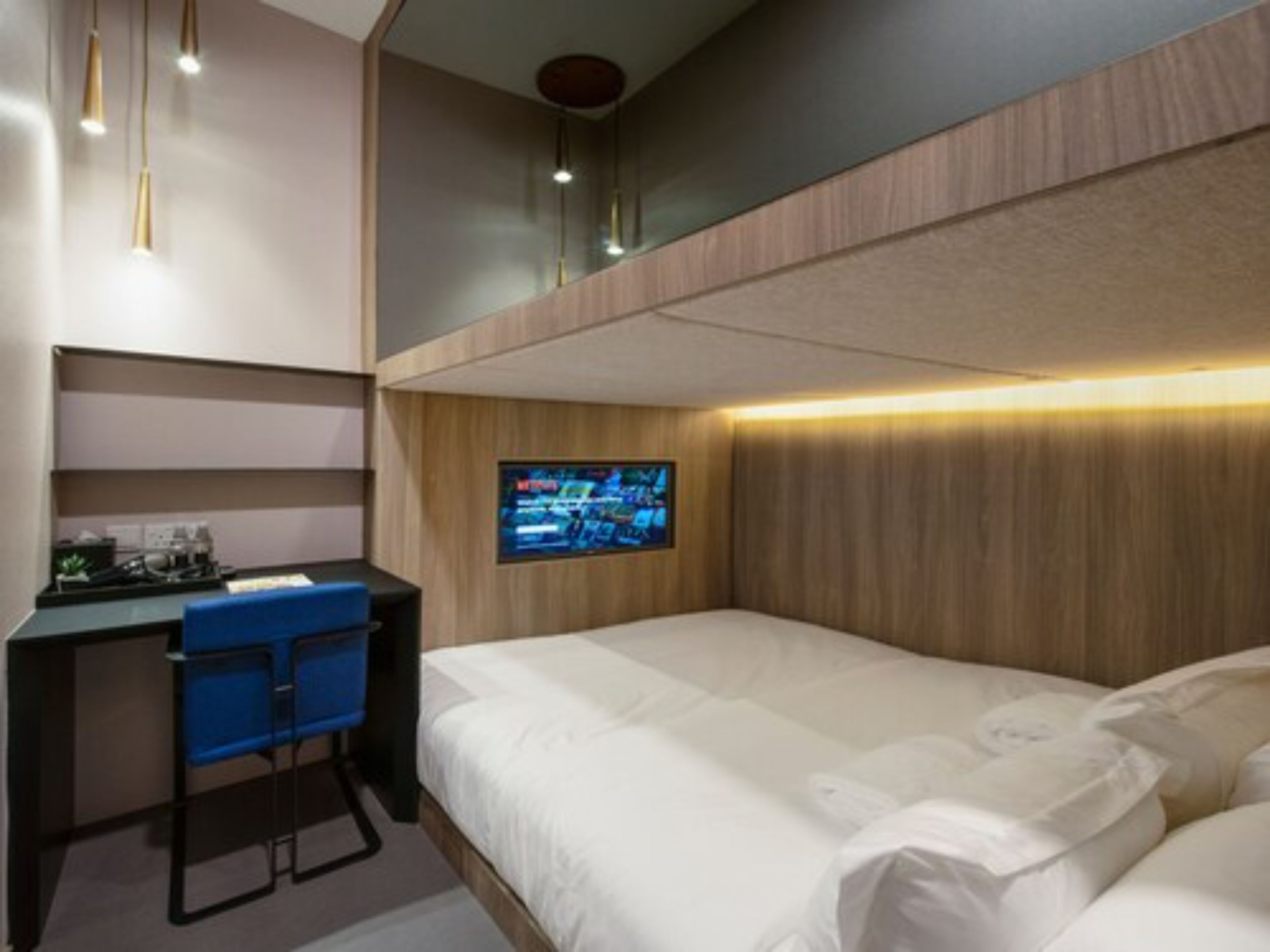Ein modernes Hotelzimmer mit einem Bett, einem Schreibtisch und einem an der Wand befestigten Fernseher.