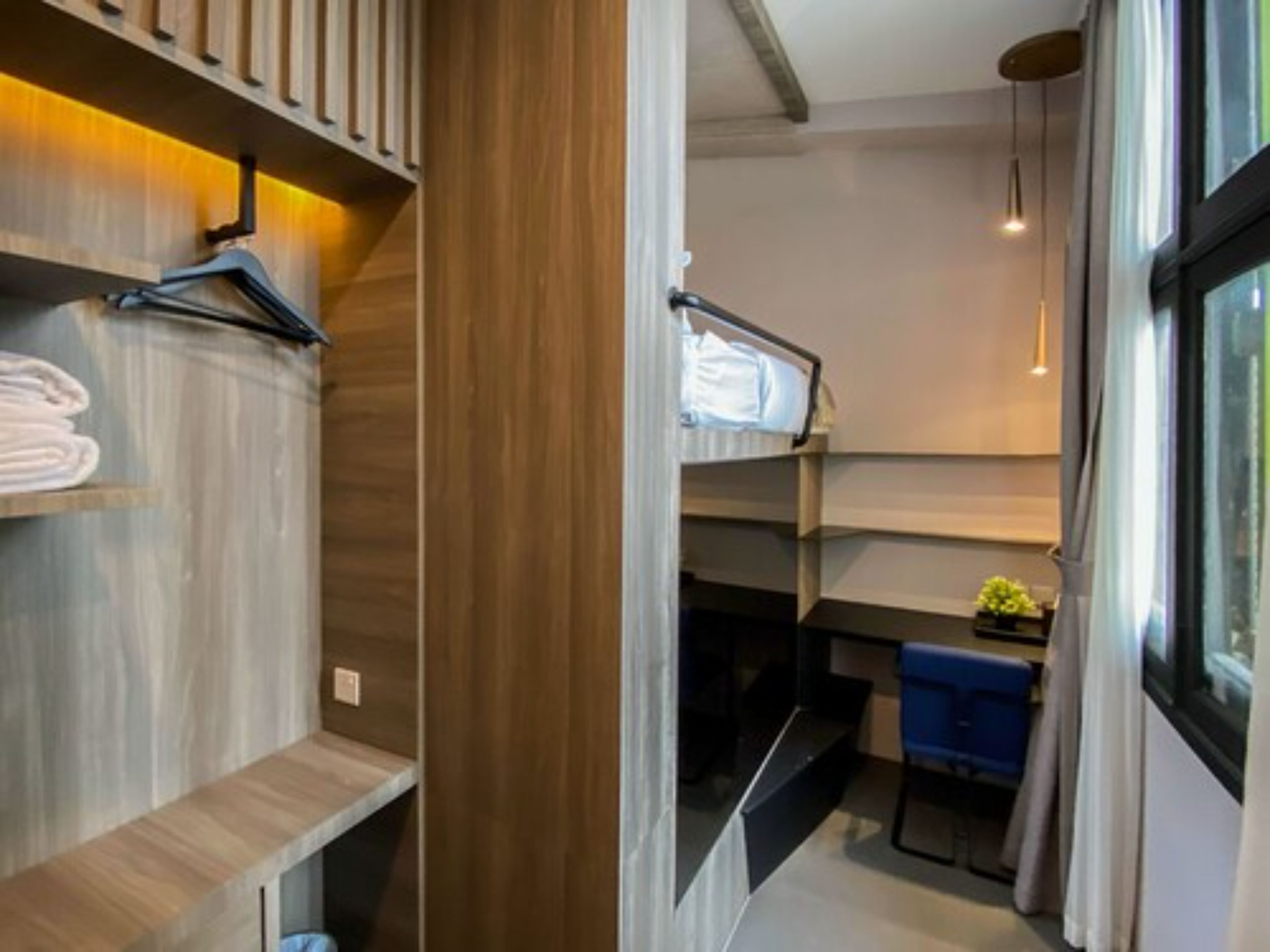 Una habitación de hotel moderna con una litera, estanterías de madera, un escritorio y una ventana con cortinas.