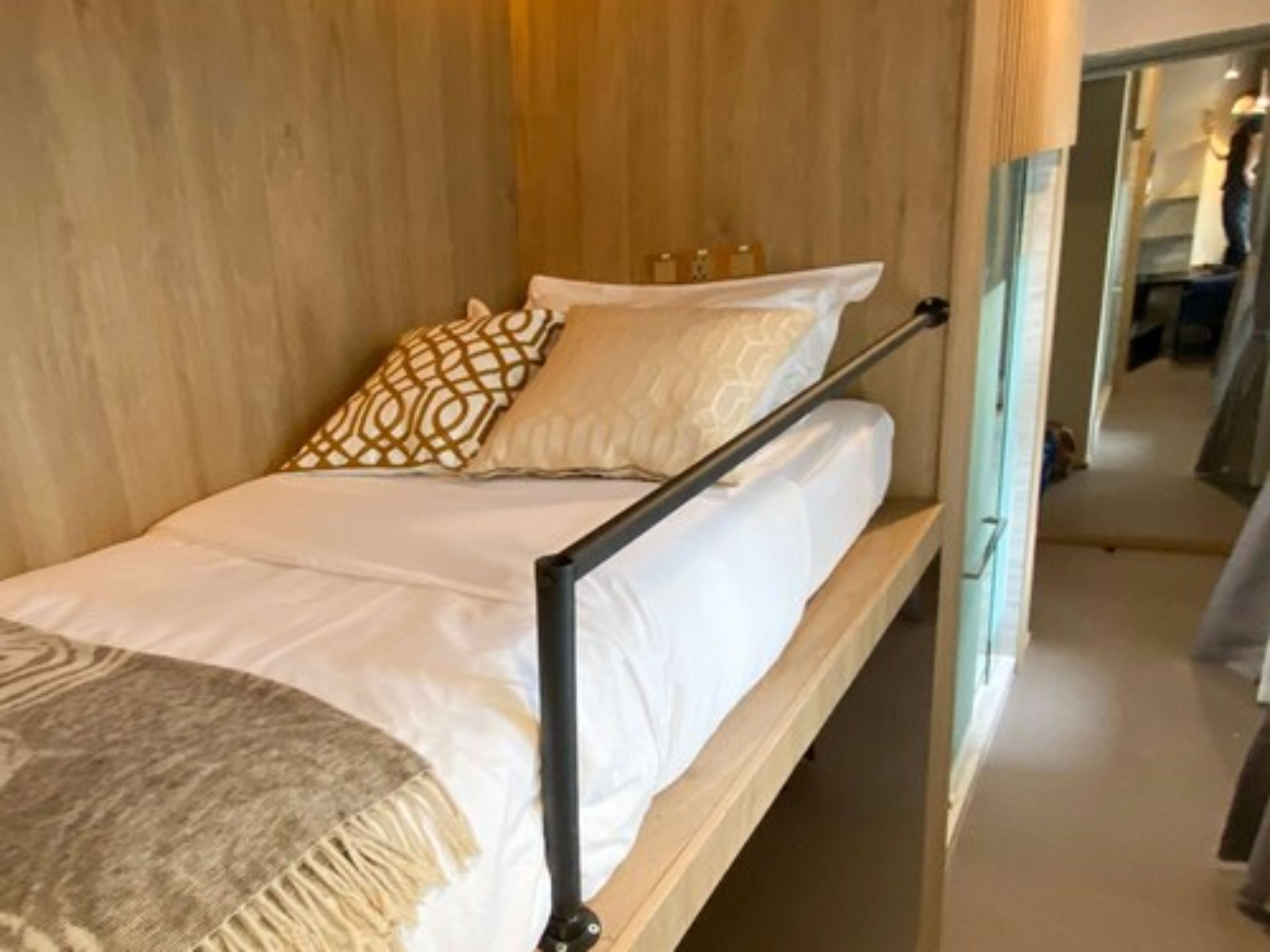 A single bed with a wooden frame, white bedding, and patterned pillows.