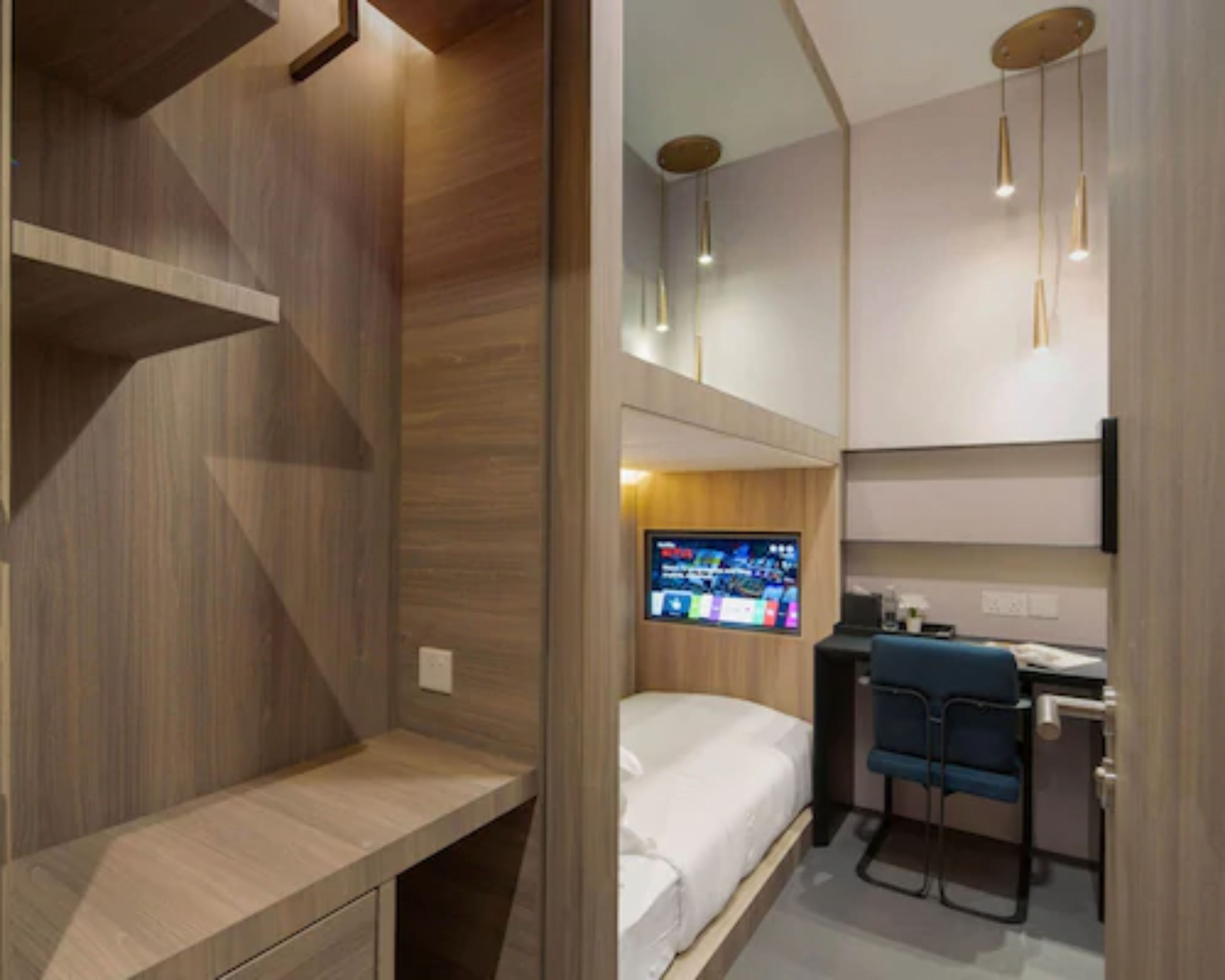 A compact room with a bed, a desk, and a TV mounted on the wall.