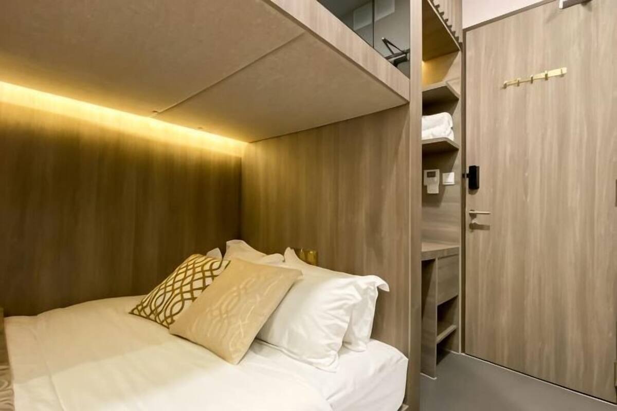 A hotel room with a bed, wooden headboard, built-in wardrobe, and a shelf with towels.