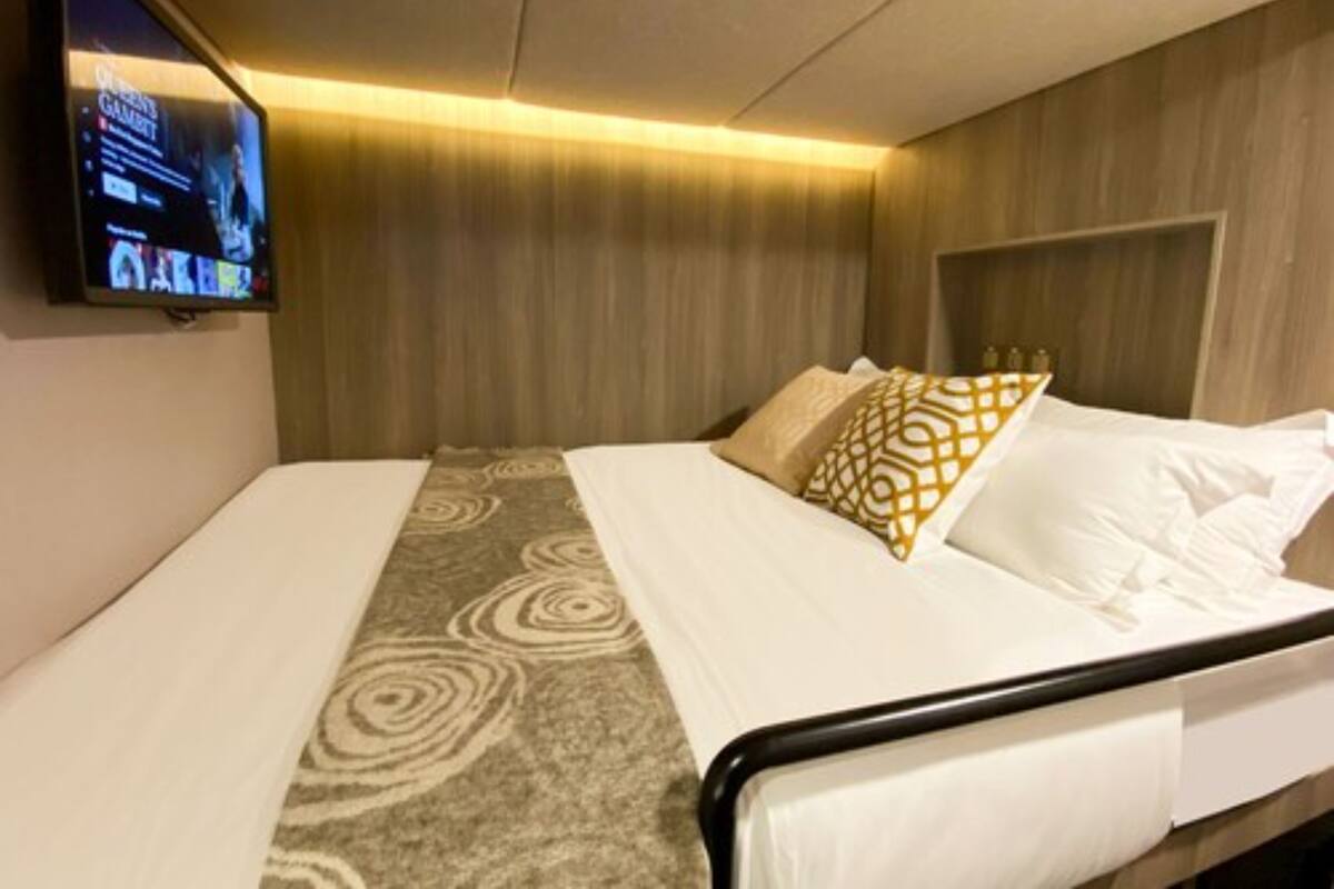 A hotel room with a bed, a TV mounted on the wall, and a wooden headboard.