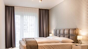 A modern bedroom with a large bed, a geometric patterned wall, a ceiling light fixture, and a nightstand with a lamp.