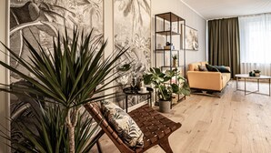 Uma sala de estar moderna com um banco de madeira, um sofá e uma mesa de centro. Há várias plantas em vasos e uma estante de livros.