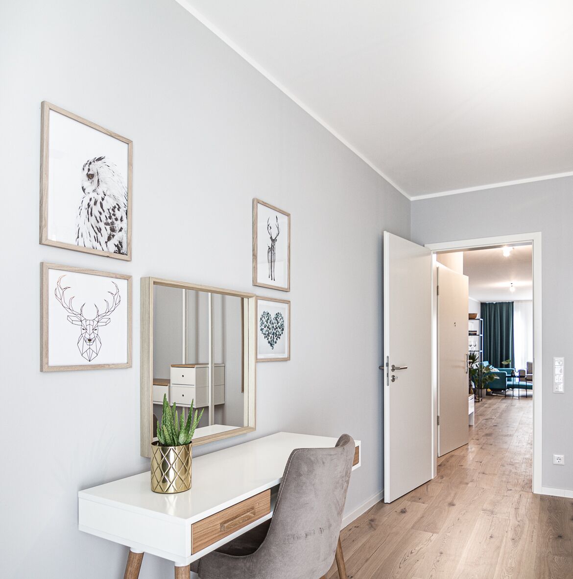 Ein modernes Zimmer mit einem weißen Schreibtisch, einem großen Spiegel und gerahmten Kunstwerken an der Wand.