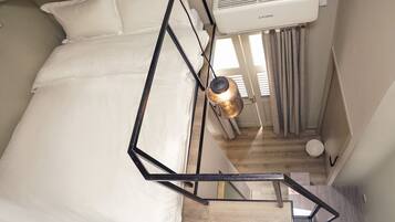 A bedroom with a bed, a hanging light fixture, an air conditioning unit, and a view of a staircase.