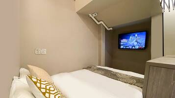 A hotel room with a bed, a television mounted on the wall, and a small cabinet.