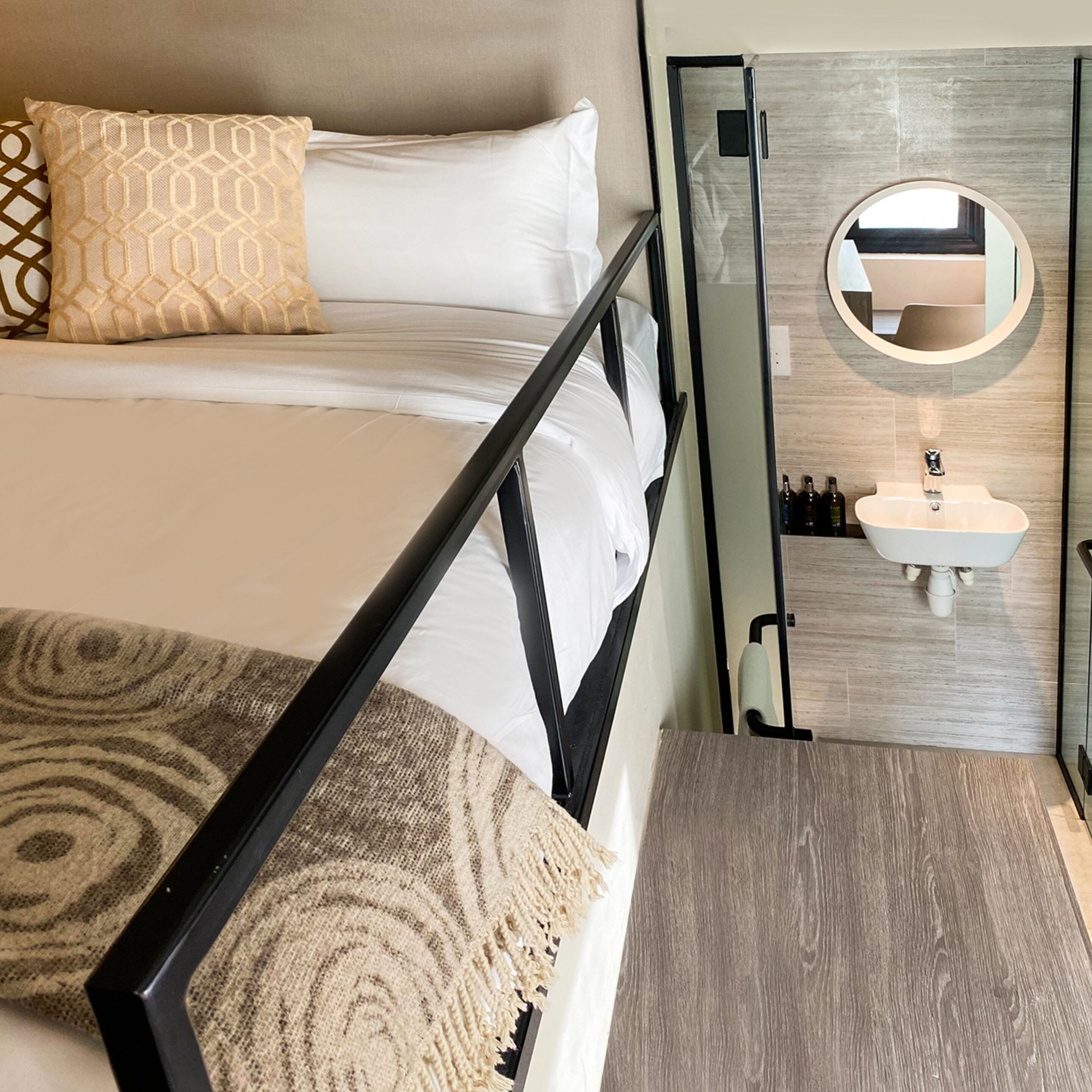 A neatly arranged bedroom with a bed, a bedside table, a mirror, and a small sink.