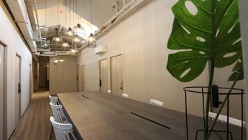 A conference room with a long table, white chairs, and a large green plant.
