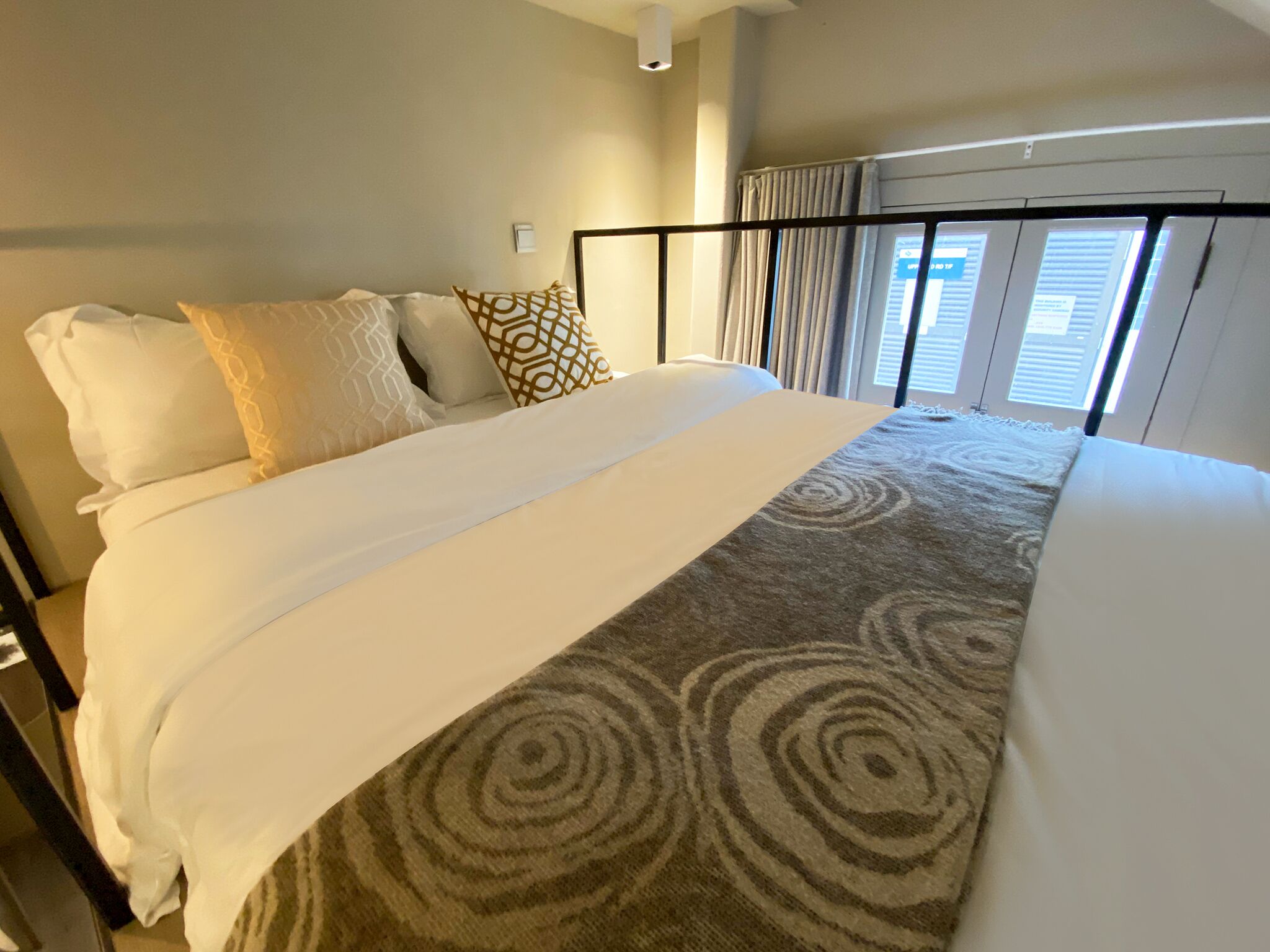Habitación de hotel con una cama grande, vistas de la ciudad a través de la ventana y una lámpara en el techo.