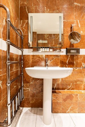 A bathroom with a marble wall, a white sink, a mirror, and a towel rack. - Cockspur Street by Onefinestay (London)