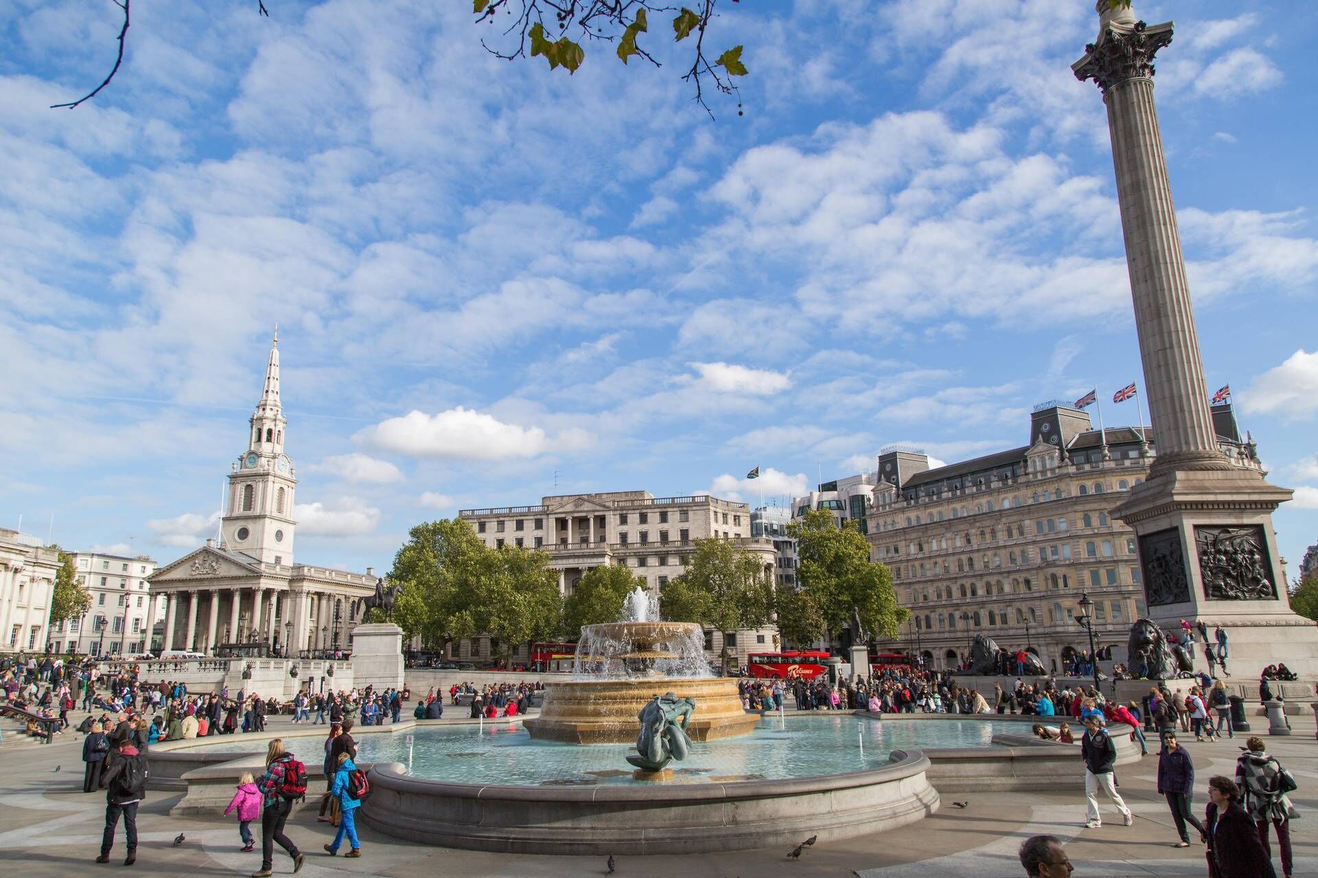 A public square with a central fountain, a tall column, and a historic building with a clock tower.