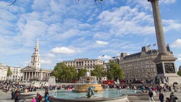 A public square with a central fountain, a tall column, and a historic building with a clock tower.