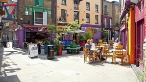A street with outdoor seating, a sign for 'Meals Yard Deli', and a 'New Organic Make-Up' advertisement. - Cockspur Street by Onefinestay (London)