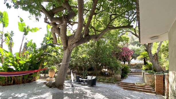 A patio with a hammock, outdoor furniture, and a gravel path leading to a stone wall. - Dimora Tana Pacenzia (Cefalù)