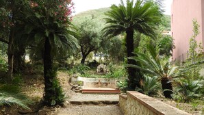 A garden with a stone wall, palm trees, and a concrete bench. - Dimora Tana Pacenzia (Cefalù)
