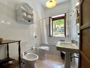 Casa de banho com bidé, sanita, lavatório e janela com vista para o verde.